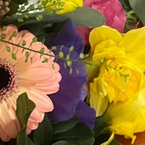 Anémone bleu-violet vue de côté dans un bouquet, entre un gerbera saumon et des narcisses doubles jaunes
