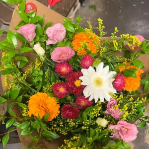 Bouquet rond mêlant zinnias orange, reines-marguerites roses, gerbera blanc, roses et solidage sur papier kraft