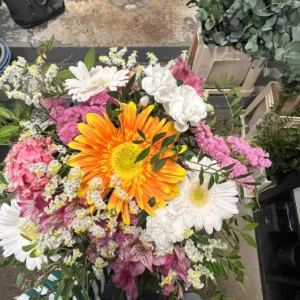 Bouquet de saison autour d'un grand gerbera orange, avec matricaire blanche, œillets blancs et fleurs roses en grappes