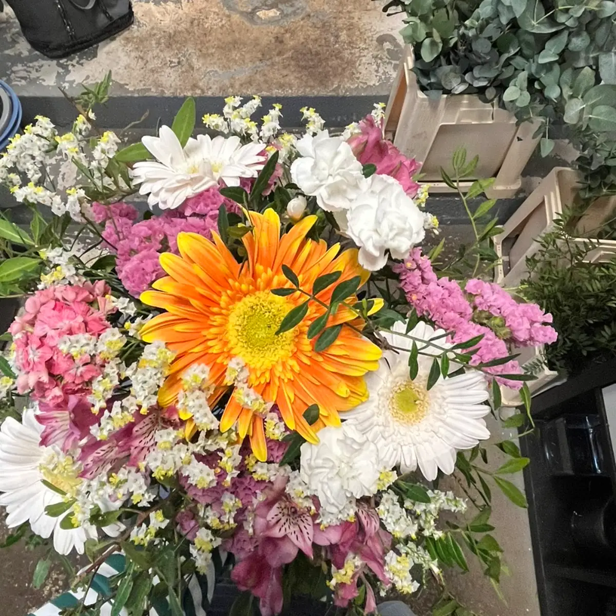Bouquet de saison autour d'un grand gerbera orange, avec matricaire blanche, œillets blancs et fleurs roses en grappes