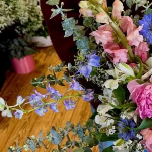 Rameau de delphinium bleu clair étalé en travers d'un bouquet, à côté de mufliers roses et de feuilles d'eucalyptus