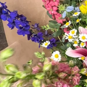 Épi de delphinium bleu violacé traversant un bouquet, chaque fleur montrant son éperon, parmi des marguerites blanches et un muflier rose