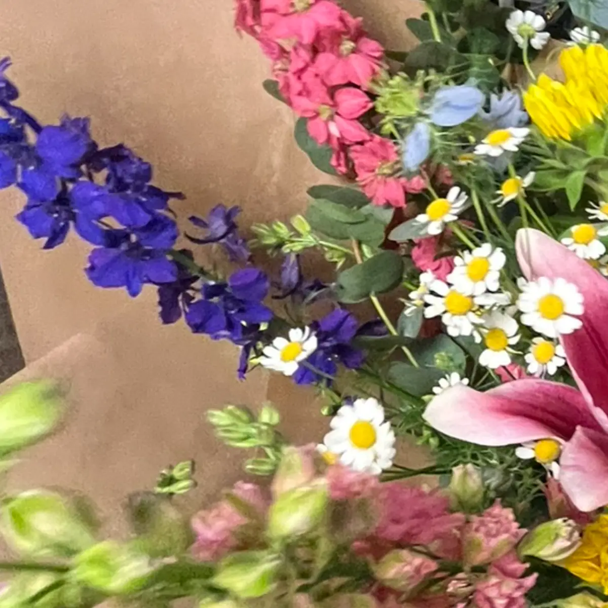 Épi de delphinium violet foncé traversant en diagonale un bouquet posé sur papier kraft, entre matricaire et fleurs roses
