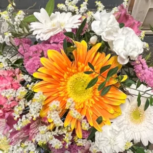 Gros plan sur un gerbera orange et jaune au cœur vert clair, entouré d'un œillet blanc, de fleurs roses et d'un petit gerbera blanc