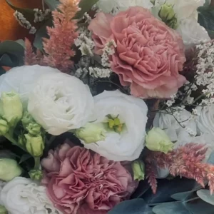 Lisianthus blanc double entièrement ouvert au centre d'un bouquet, son cœur vert et jaune bien visible, entre deux œillets rose ancien