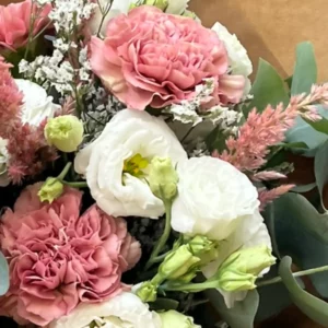 Lisianthus blanc grand ouvert au cœur jaune, entouré d'œillets rose ancien et de boutons encore fermés