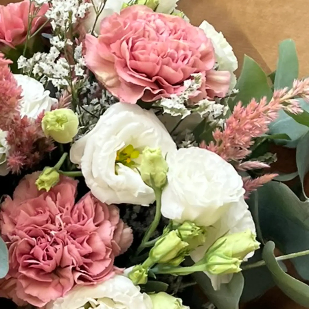 Lisianthus blanc grand ouvert au cœur jaune, entouré d'œillets rose ancien et de boutons encore fermés