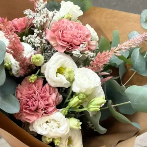 Bouquet en papier kraft où des lisianthus blancs voisinent avec des œillets roses, de la célosie et de l'eucalyptus