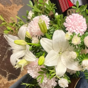 Lys blancs épanouis et boutons fermés dans un bouquet, entourés de reines-marguerites roses