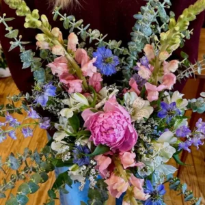 Bouquet où deux épis de muflier saumon et crème encadrent une pivoine rose, avec nigelles bleues et eucalyptus