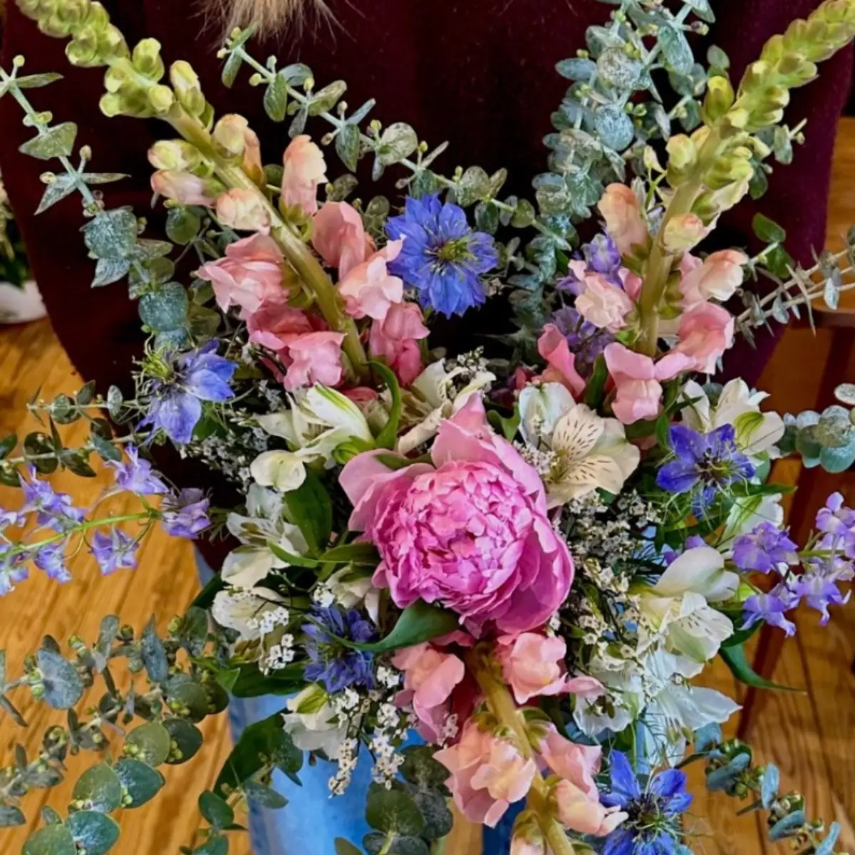 Bouquet où deux épis de muflier saumon et crème encadrent une pivoine rose, avec nigelles bleues et eucalyptus