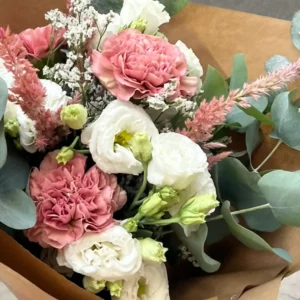 Trois œillets rose ancien aux pétales frangés, serrés entre des lisianthus blancs et de l'eucalyptus dans un bouquet en papier kraft