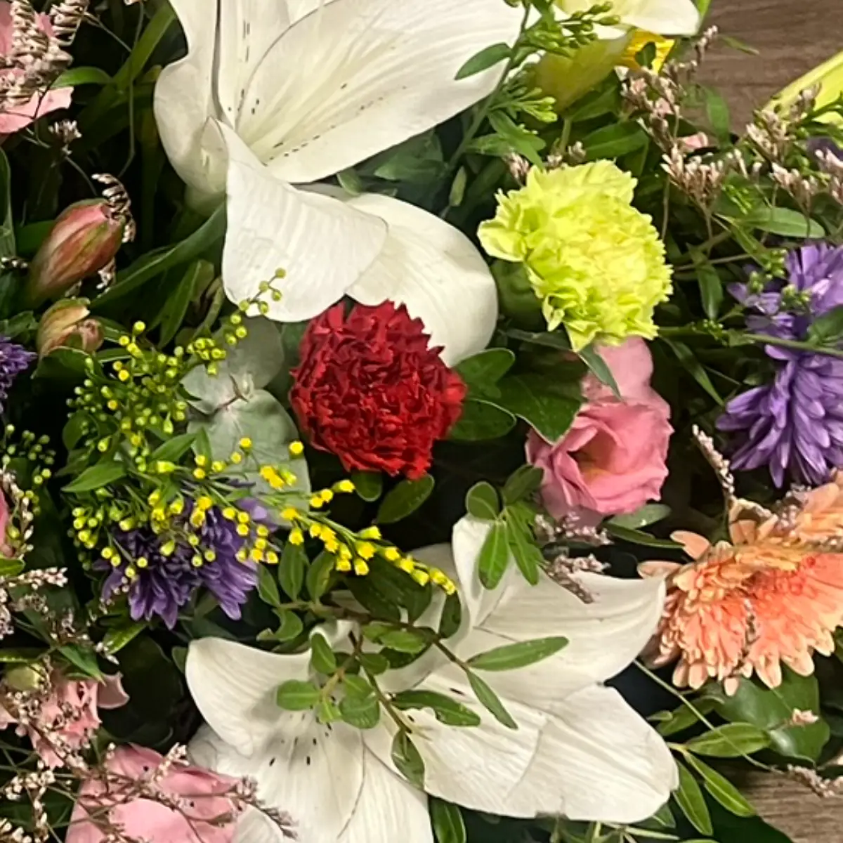 Un œillet rouge sombre et un œillet vert anis côte à côte dans une composition, entourés de lys blancs et d'asters violets